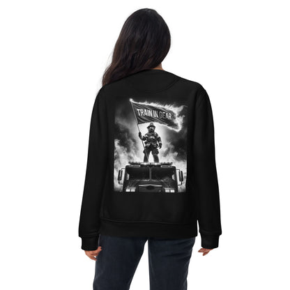 Train in Gear Firefighter graphic sweatshirt long sleeve in black. Black and white image of a firefighter standing on a fire truck, holding up a burning flag that reads "Train in Gear".