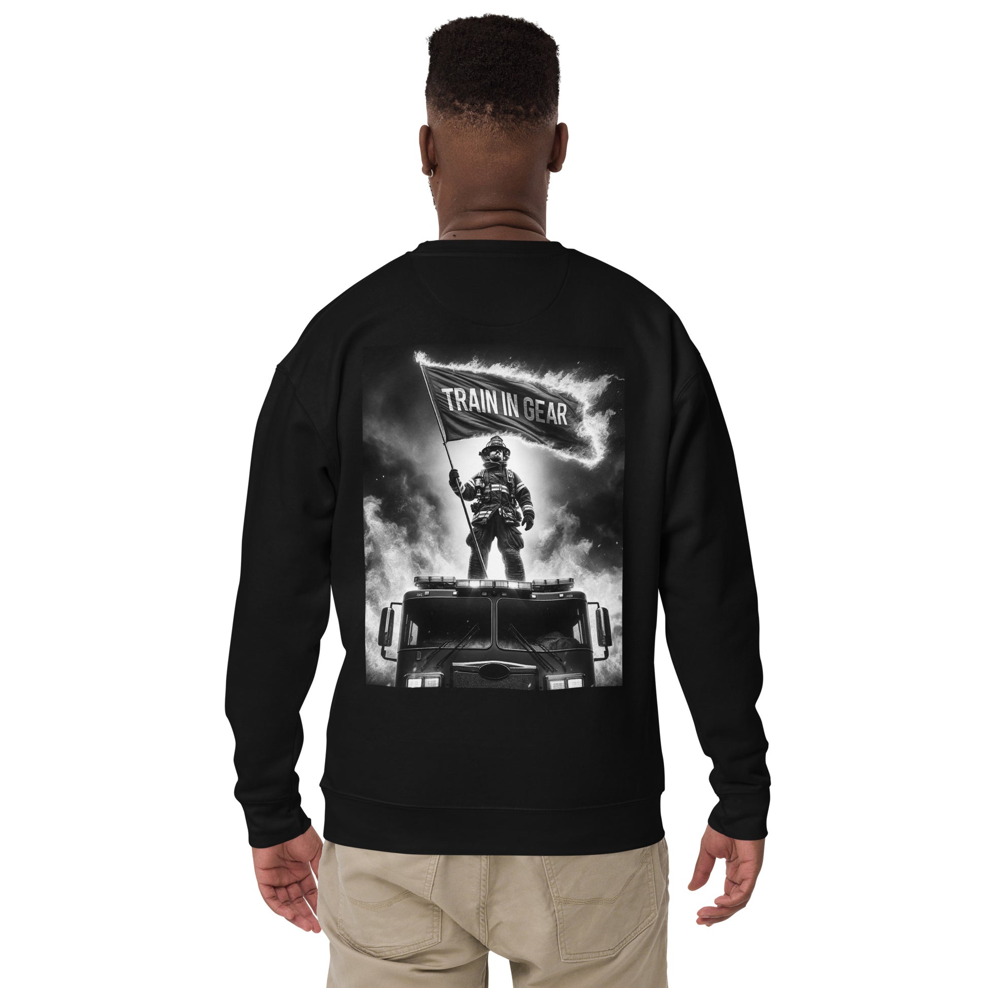 Train in Gear Firefighter graphic sweatshirt long sleeve in black. Black and white image of a firefighter standing on a fire truck, holding up a burning flag that reads "Train in Gear".